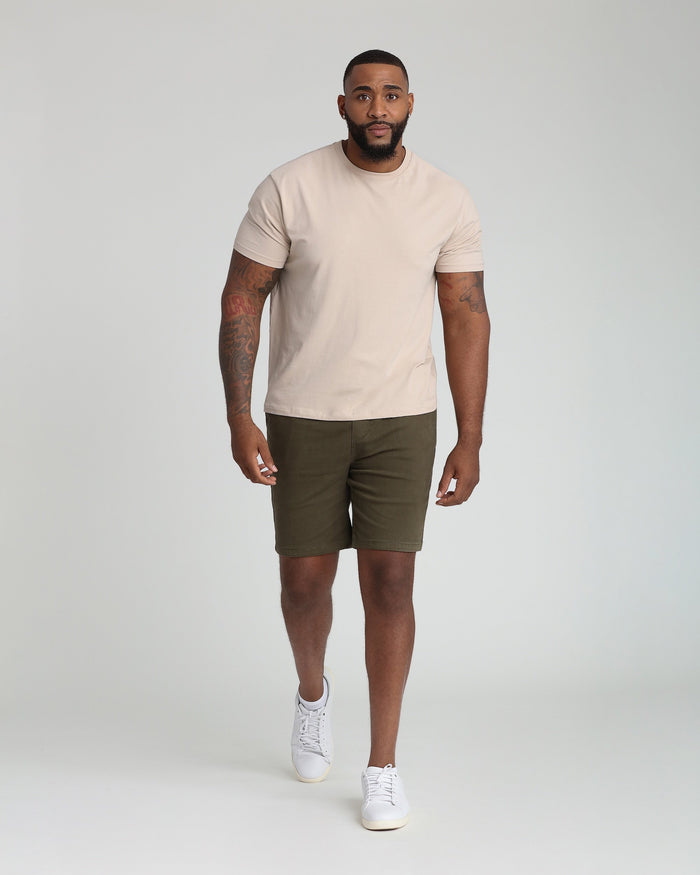 Man wearing soldier olive athletic fit shorts paired with a beige t-shirt and white sneakers.