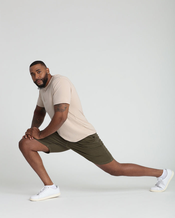 Soldier olive athletic shorts shown on model in stretched lunge pose with cream t-shirt and white sneakers.