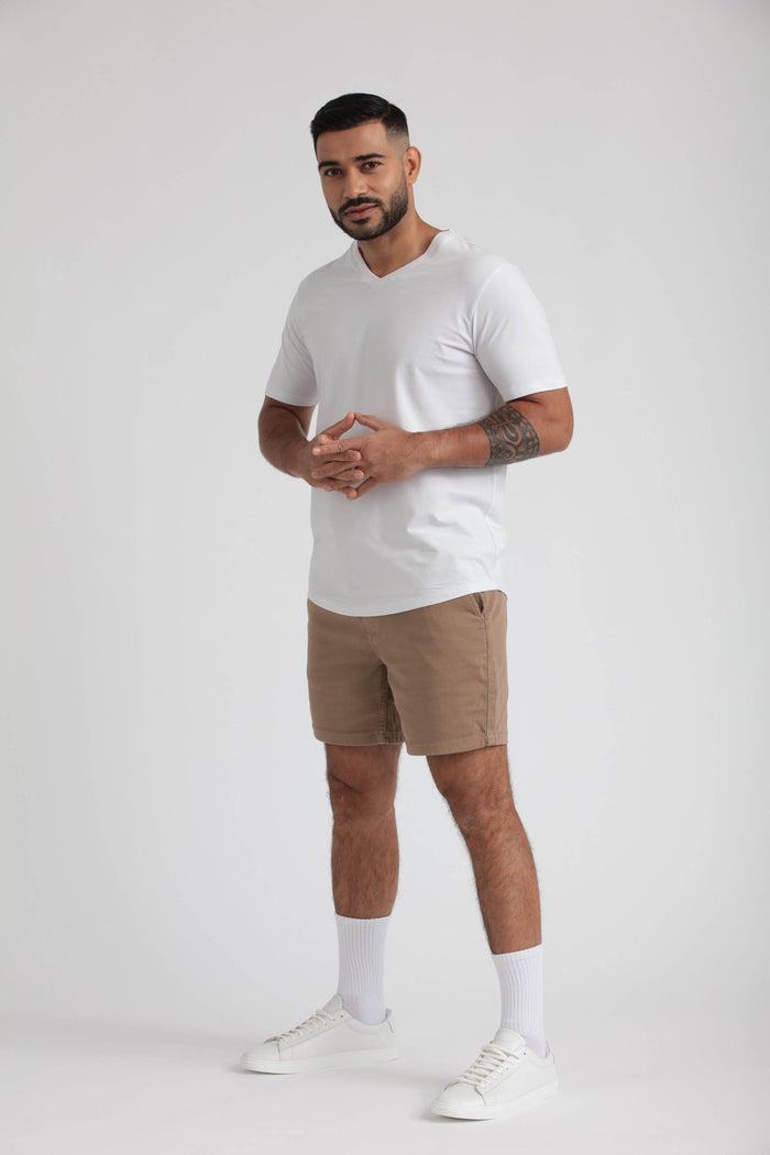 Man wearing white v-neck t-shirt and tan slim-fit shorts with white socks and white sneakers.