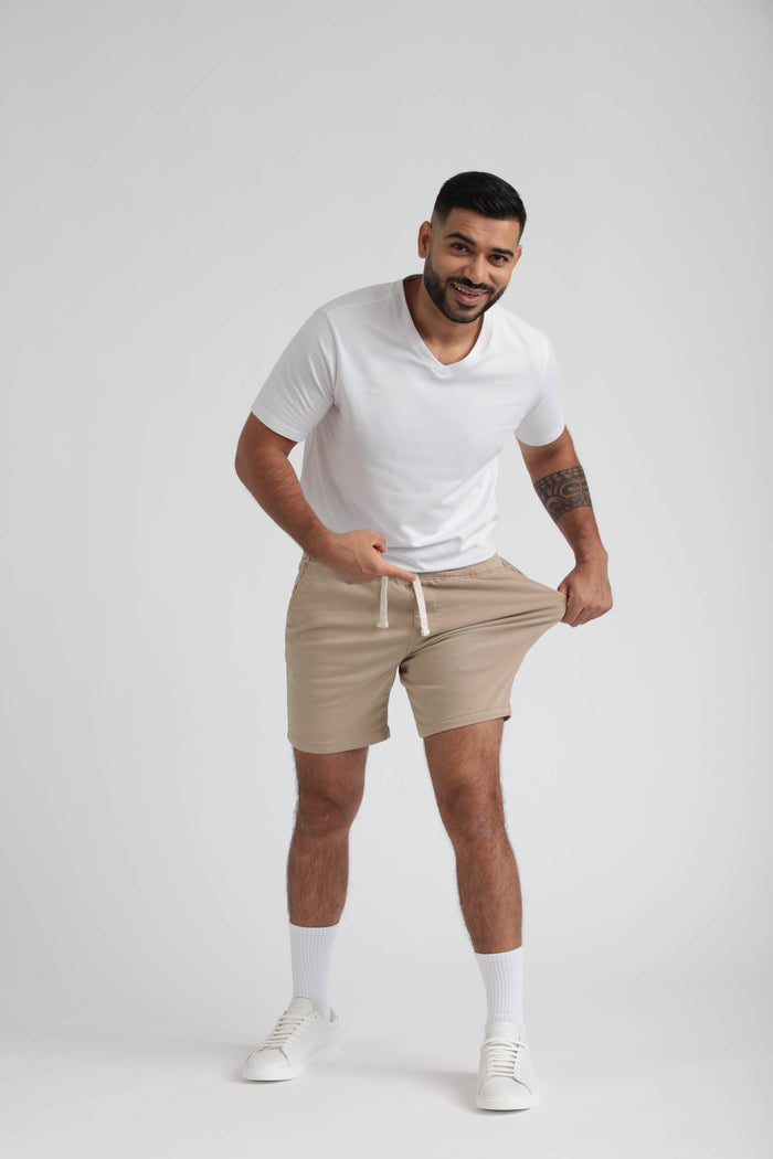 Man wearing light khaki slim fit shorts with drawstring waist and white sneakers.