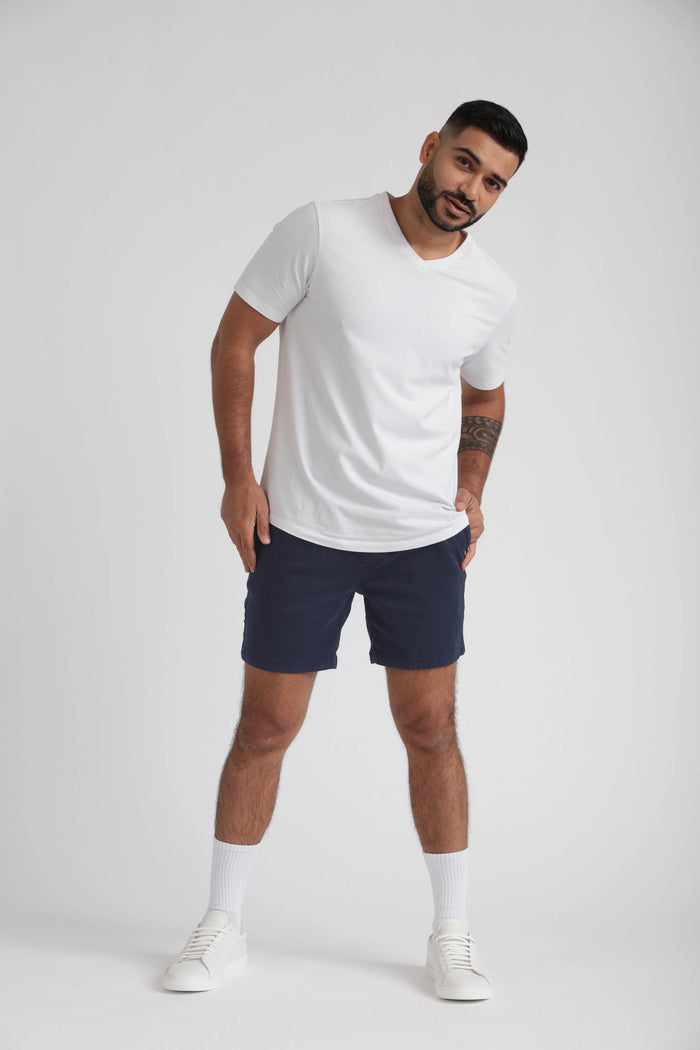 Man wearing white t-shirt and navy slim fit shorts with white socks and sneakers.