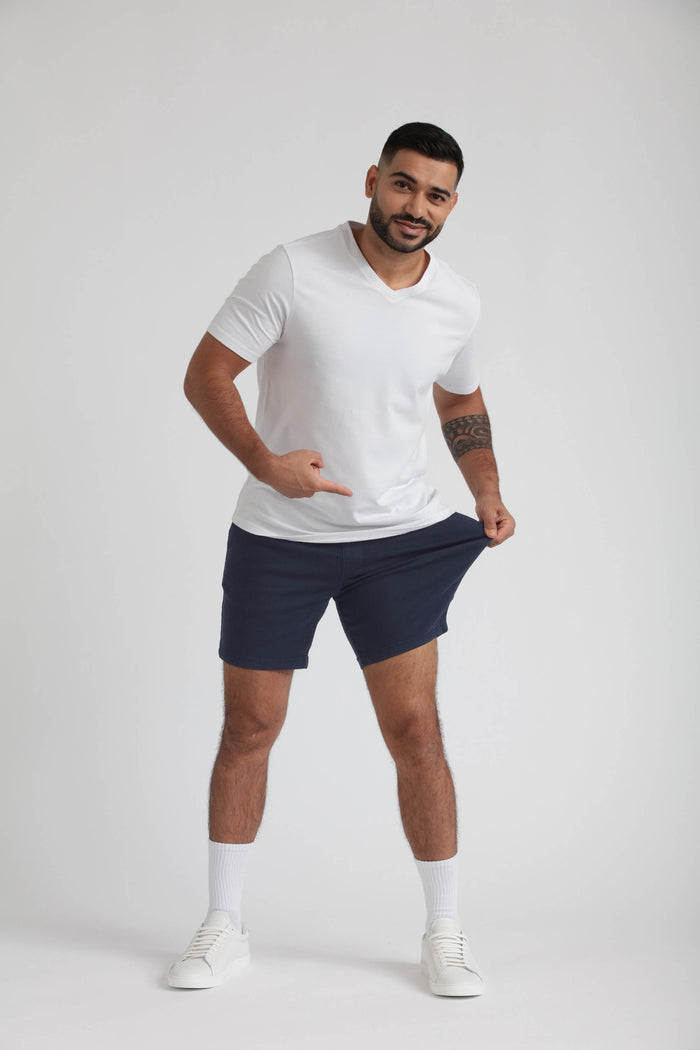 Man wearing white t-shirt and navy slim-fit shorts with white socks and sneakers.