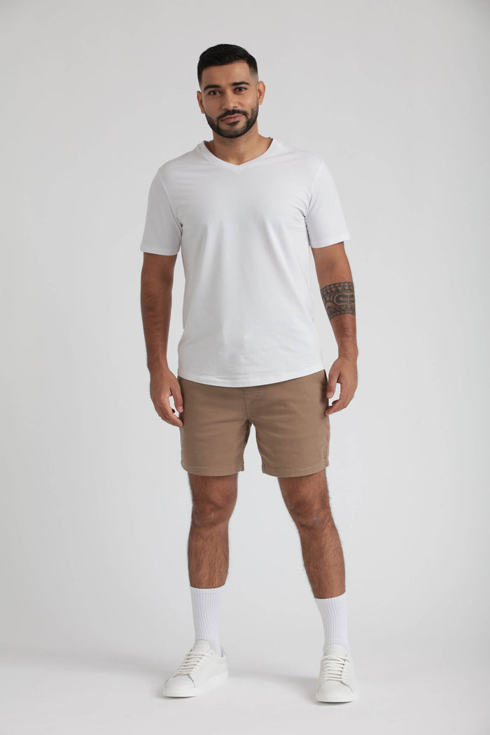 Man wearing white v-neck t-shirt and dark khaki slim fit shorts with white socks and sneakers.