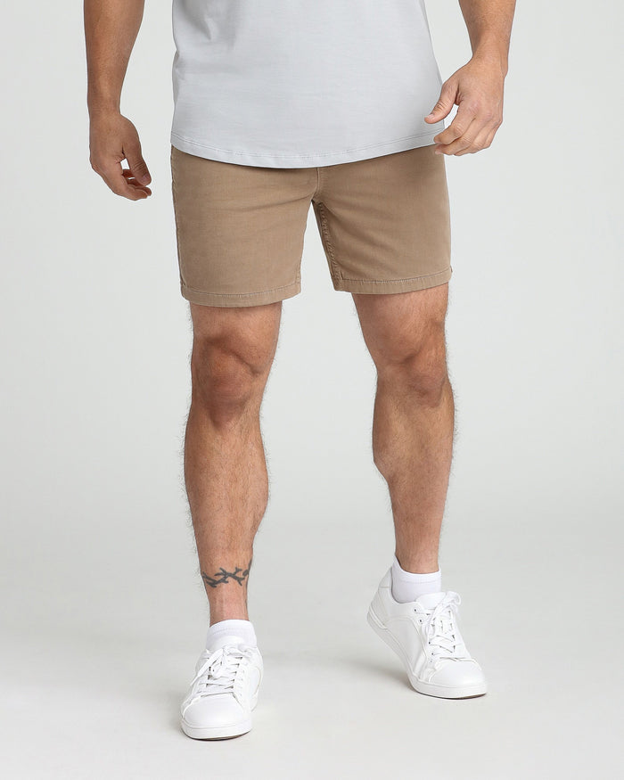 Dark khaki slim-fit shorts on a man wearing a white t-shirt and white sneakers.