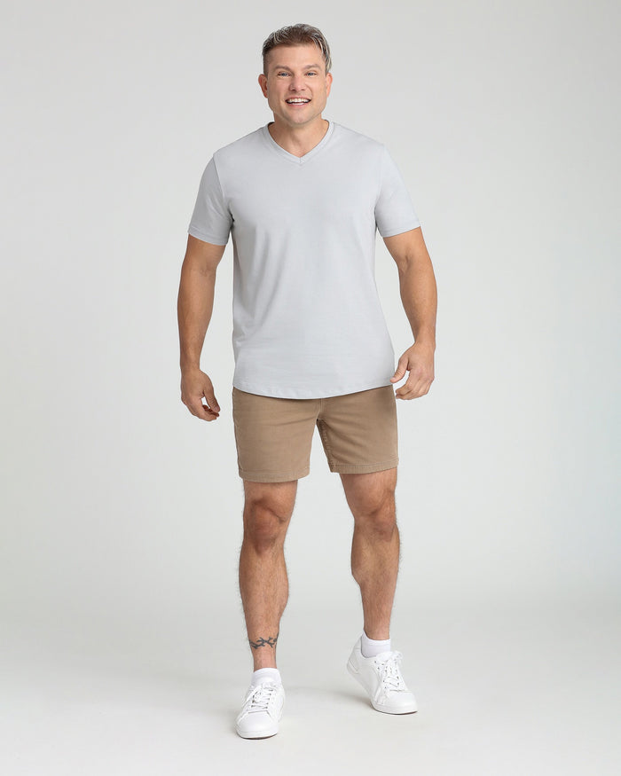 Man wearing white v-neck t-shirt and dark khaki slim fit shorts with white sneakers.