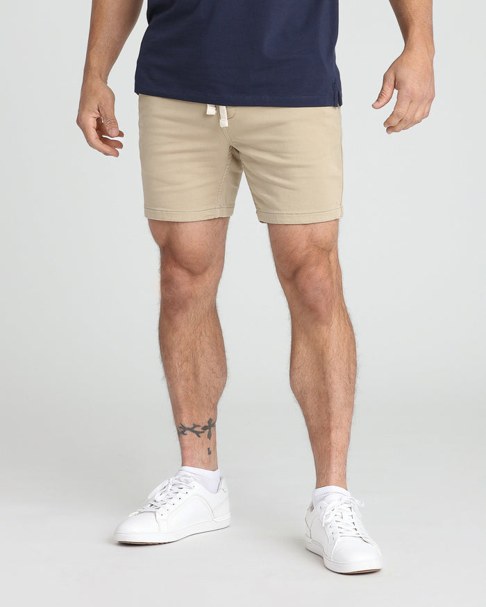 Man wearing light khaki slim fit shorts with drawstring waist and white sneakers.