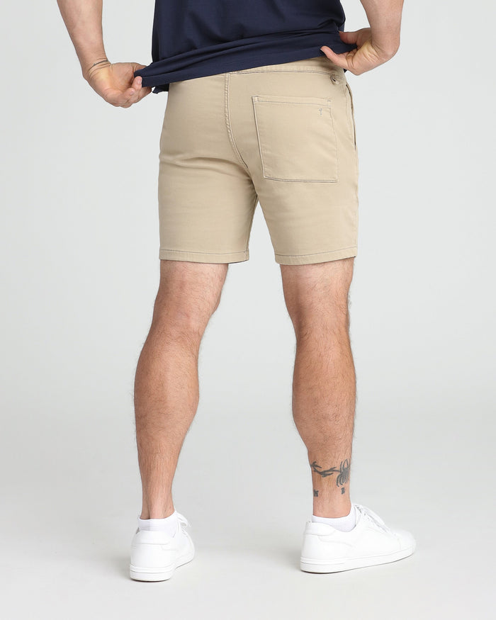Light khaki slim fit shorts with back pocket detail, worn with navy shirt and white sneakers.