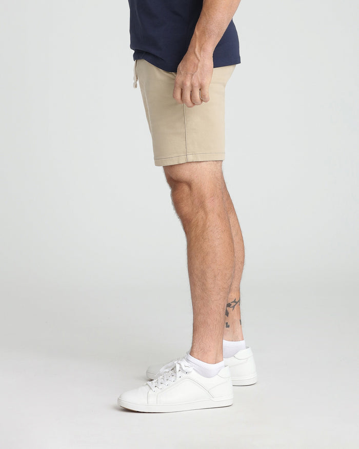 Light khaki slim-fit shorts with drawstring waist, shown on model wearing navy shirt and white sneakers.