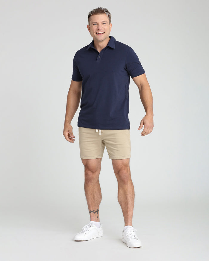 Man wearing light khaki slim fit shorts with navy polo shirt and white sneakers.