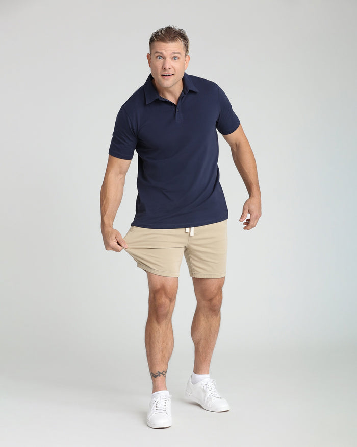 Man wearing light khaki slim fit shorts with navy polo shirt and white sneakers.