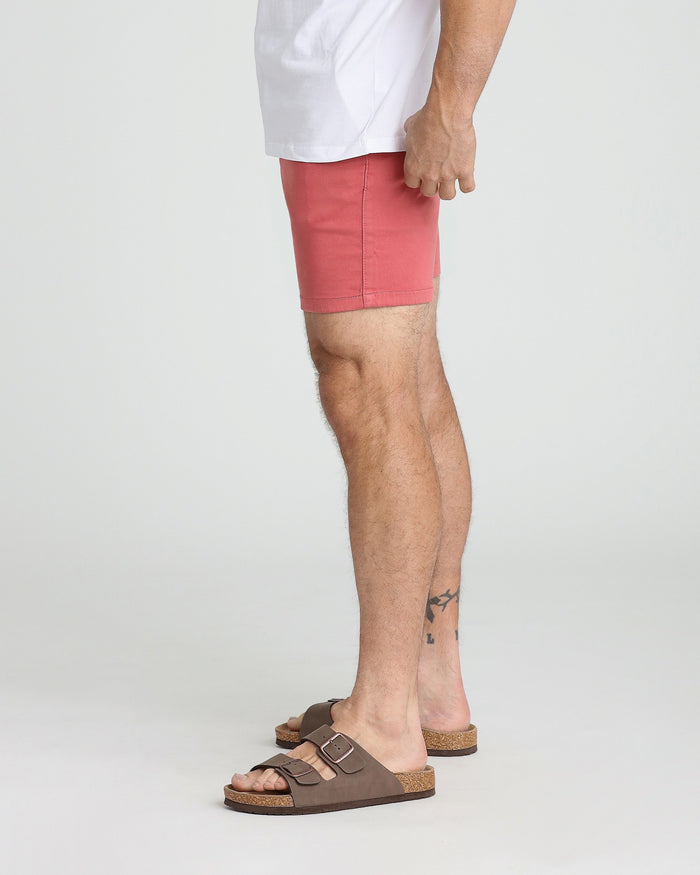Man wearing white t-shirt and coral-red slim-fit shorts with brown sandals.