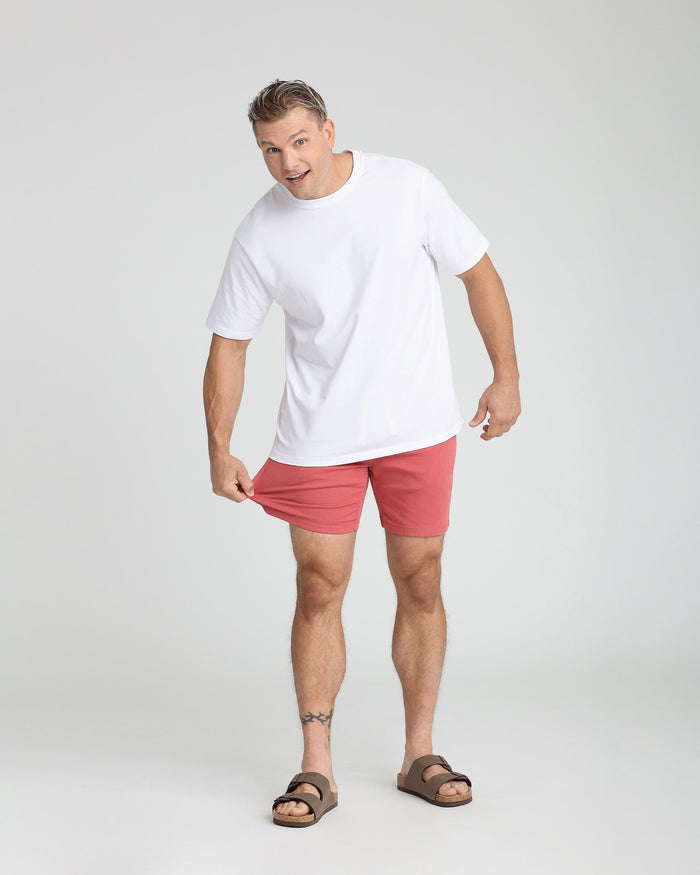 Man wearing white t-shirt and coral-red slim fit shorts with brown sandals.