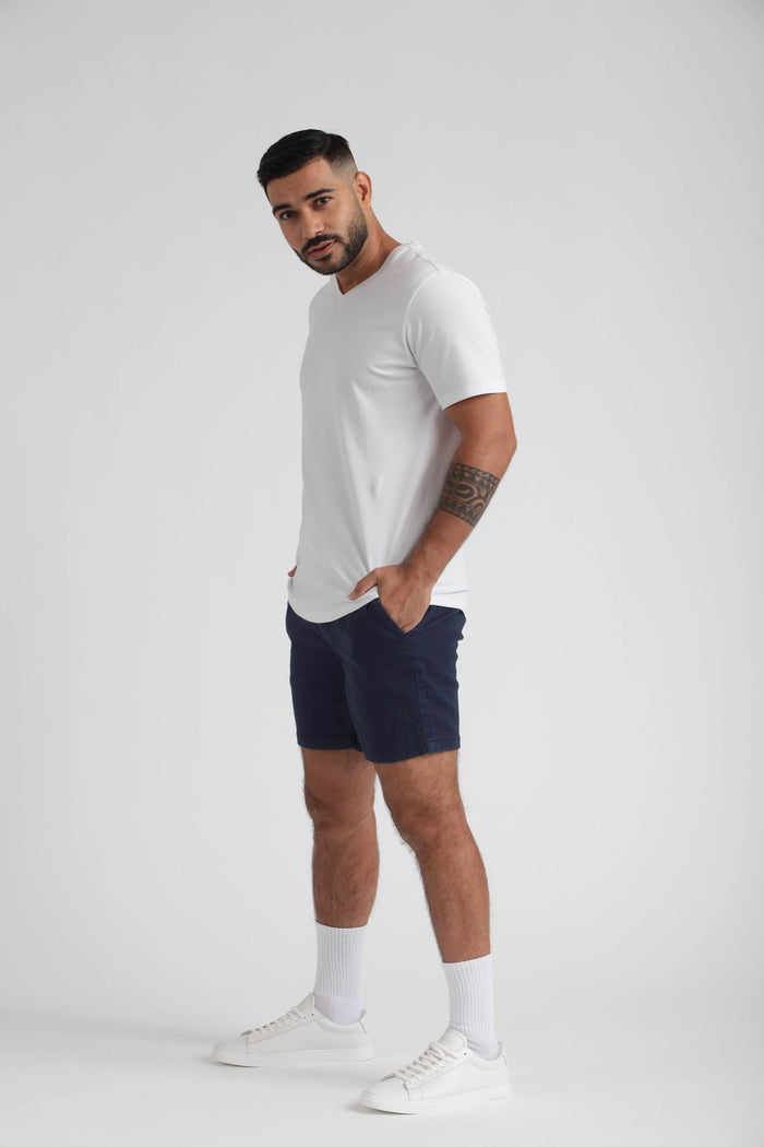 Man wearing white V-neck t-shirt and navy slim fit shorts with white socks and white sneakers.
