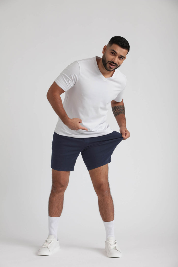 Man wearing white t-shirt and navy slim fit shorts with white socks and sneakers.