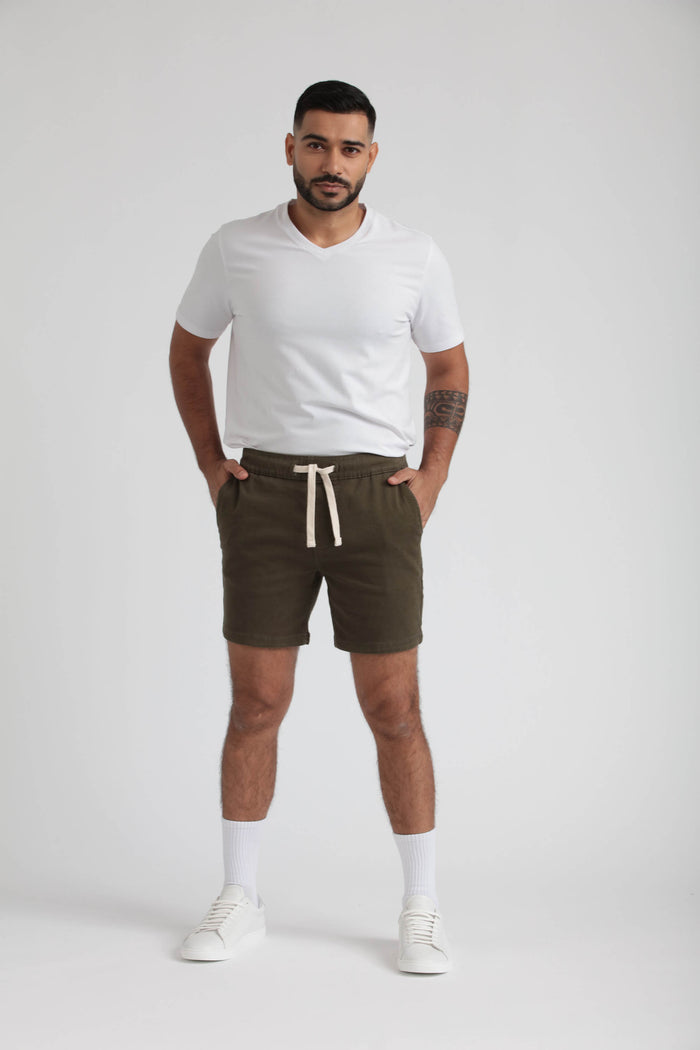 Man wearing white v-neck t-shirt and olive green slim fit shorts with drawstring waistband.