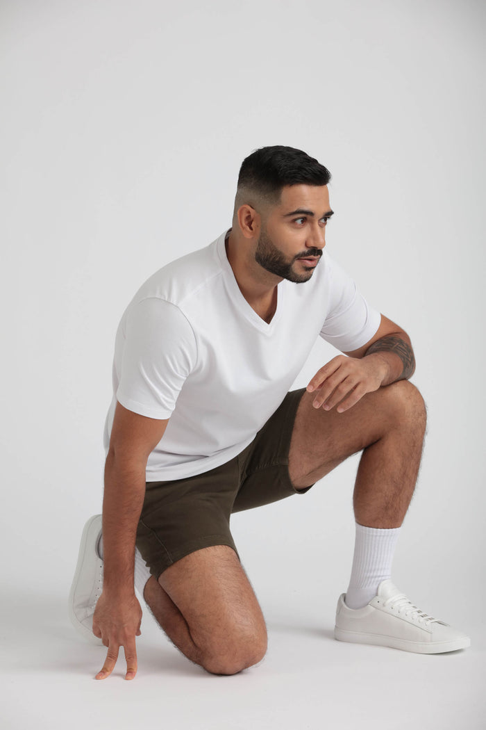 Man wearing white v-neck t-shirt and dark olive slim fit shorts with white socks and sneakers.