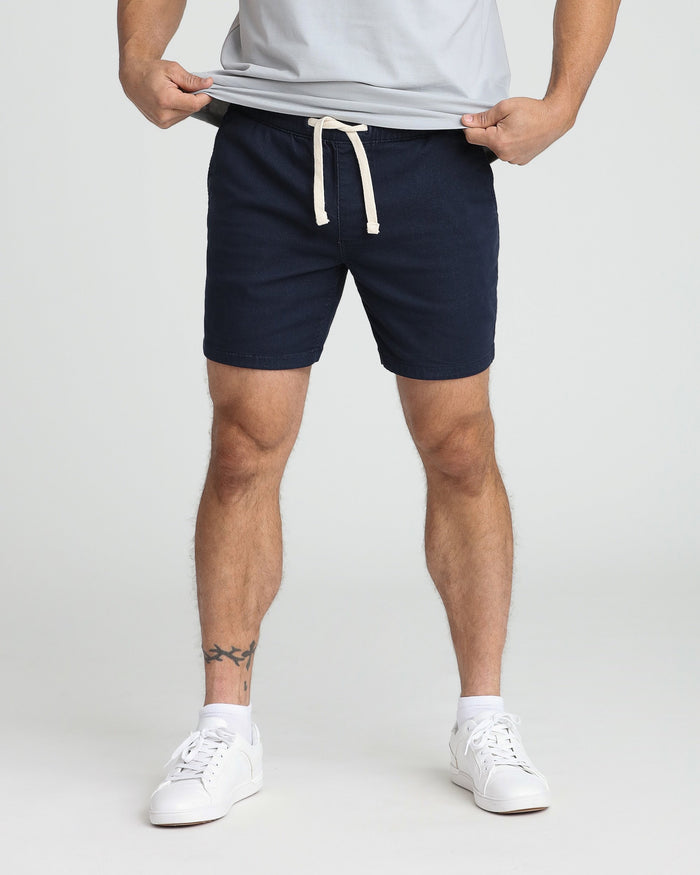 Navy slim fit shorts with drawstring waistband, shown on model wearing white t-shirt and sneakers.