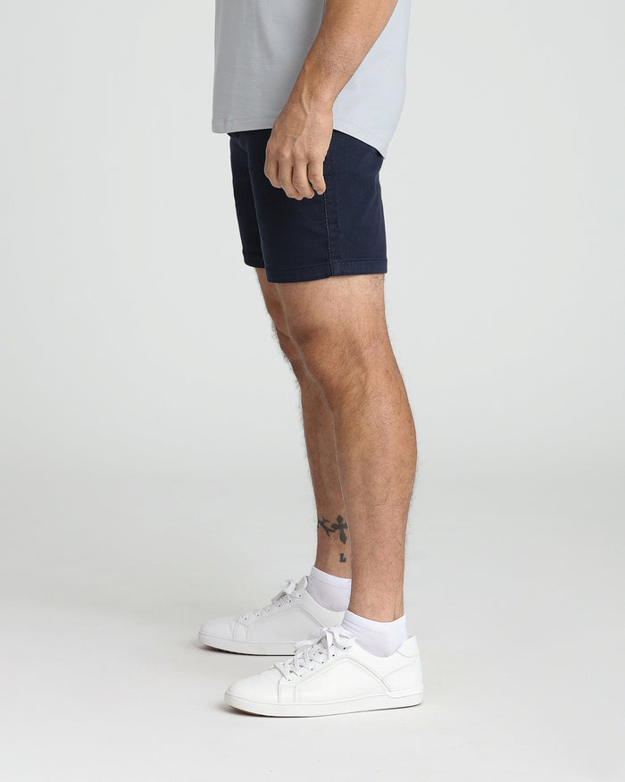 Navy slim fit shorts on model wearing light gray shirt and white sneakers.