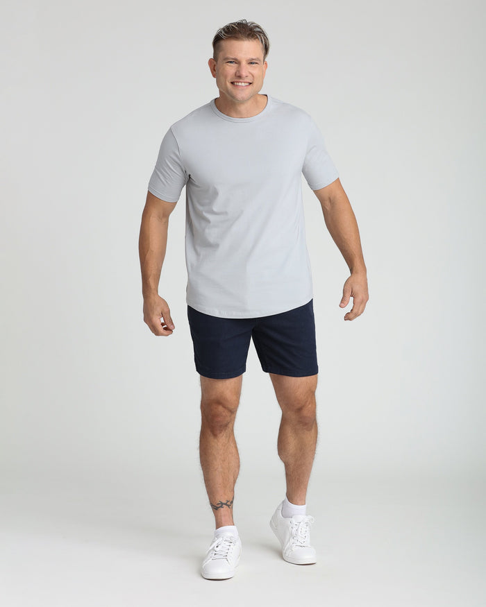 Man wearing light gray t-shirt and navy slim fit shorts with white sneakers.