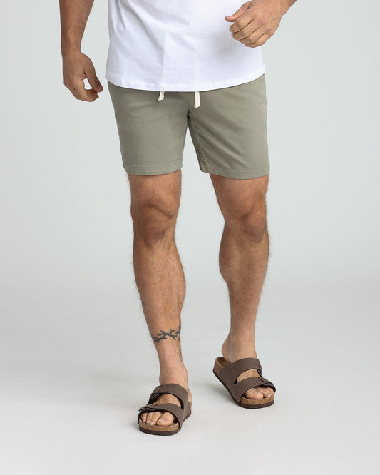 Man wearing sage green slim fit shorts with white drawstring and brown sandals.