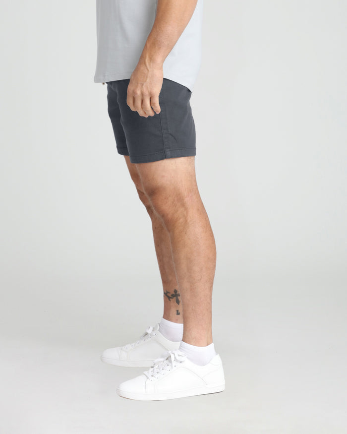 Slate-colored slim fit shorts with white sneakers and white crew socks on a male model wearing a light gray t-shirt.