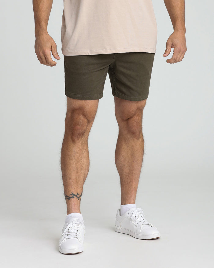 Olive green slim fit shorts on a man wearing a beige shirt and white sneakers.
