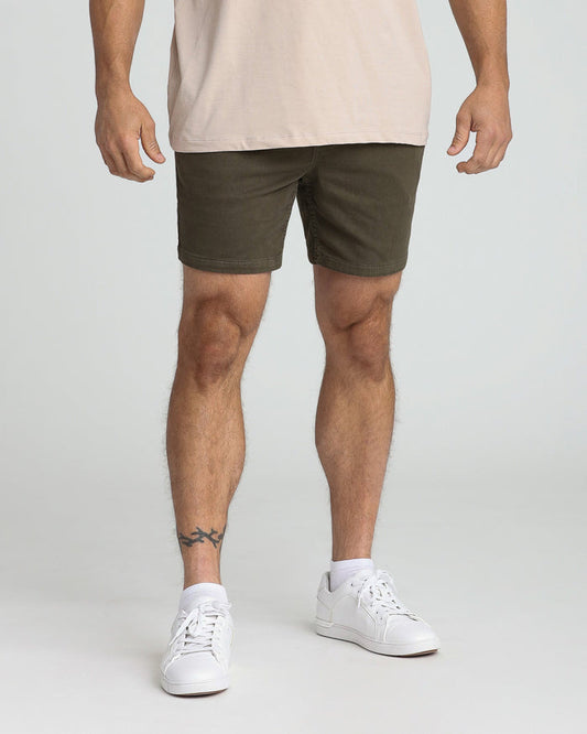 Olive green slim fit shorts on a man wearing a beige shirt and white sneakers.