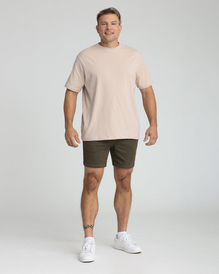 Man wearing cream t-shirt and olive green slim fit shorts with white sneakers.
