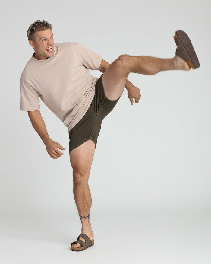 Man wearing olive green slim fit shorts with beige t-shirt and dark sandals.
