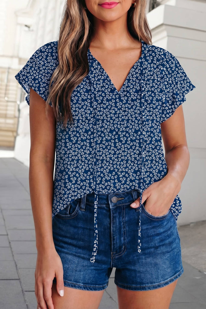 Woman wearing a blue floral top and denim shorts on a city street.