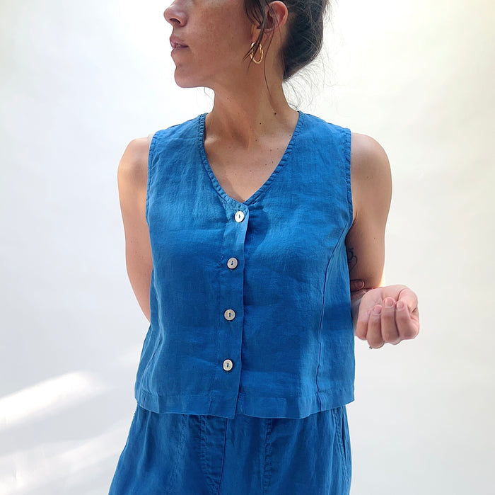 Woman wearing a blue sleeveless top with buttons against a white background