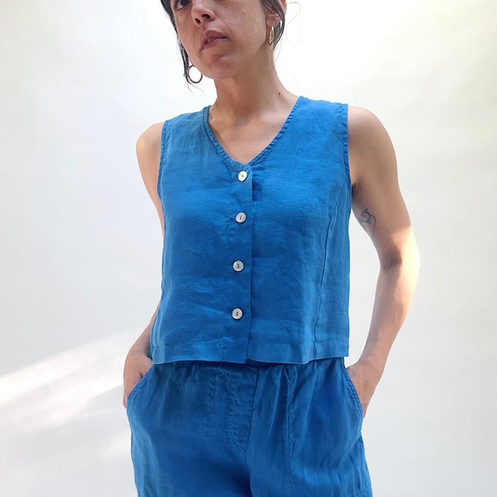 Person wearing a blue sleeveless top with buttons and matching pants against a white background