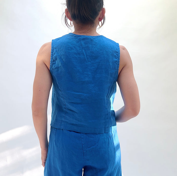 Person wearing a blue sleeveless top and pants against a white background, shot from behind.