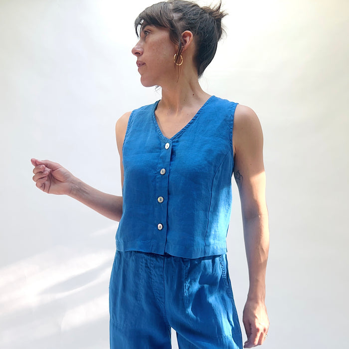 Woman wearing a blue sleeveless top and pants against a white background