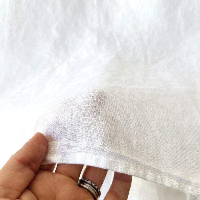 Close-up of a hand holding white fabric with visible stitching.