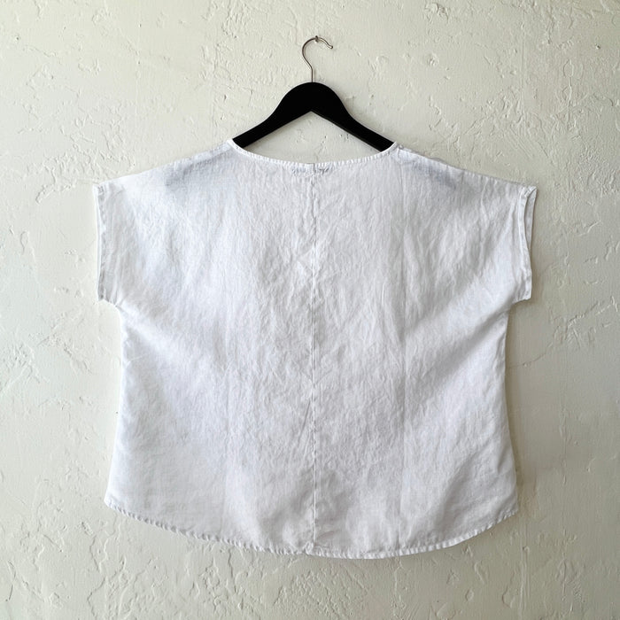 White top on a hanger against a white wall, viewed from behind
