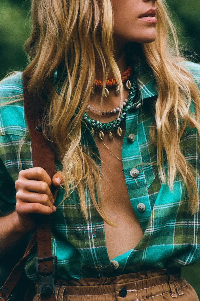 Close-up of teal green plaid flannel shirt with shell button front opening, styled with layered shell necklaces