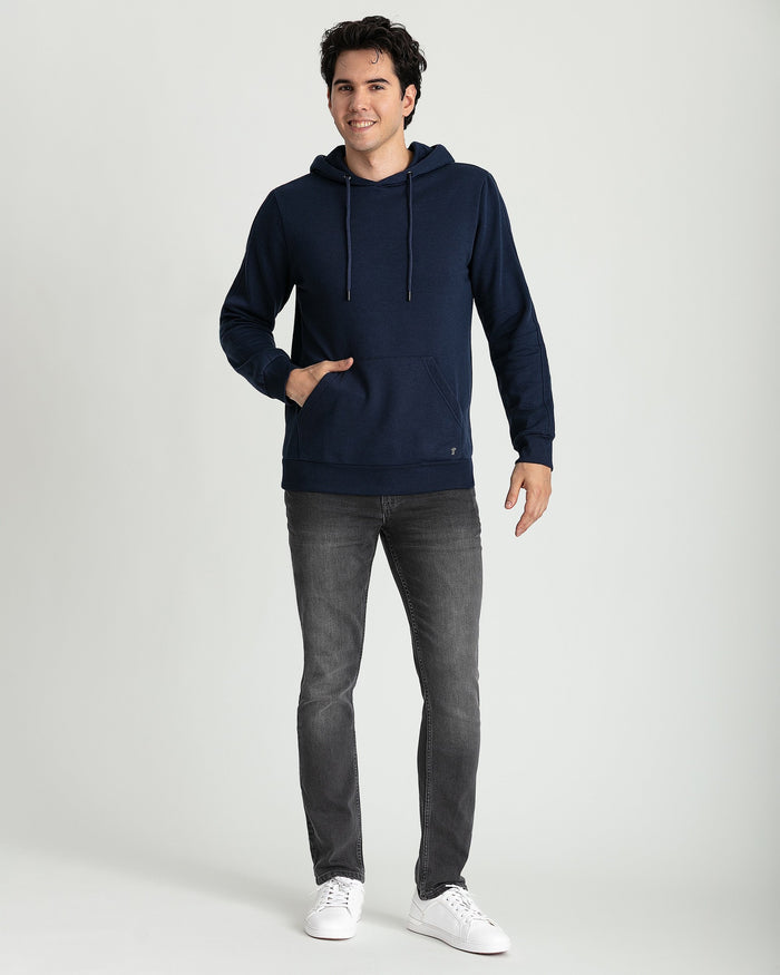 Navy pullover hoodie with drawstring hood, kangaroo pocket, and ribbed cuffs, worn with gray jeans.