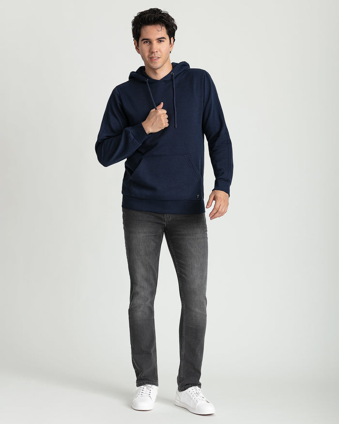 Navy hoodie with drawstring, kangaroo pocket, worn with gray jeans and white sneakers.