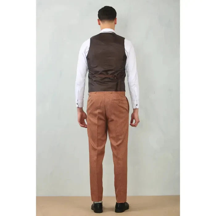 Back view of a man wearing a men's camel tailored fit wedding 3-piece suit with brown trousers, white shirt, and dark vest, standing against a plain wall.
