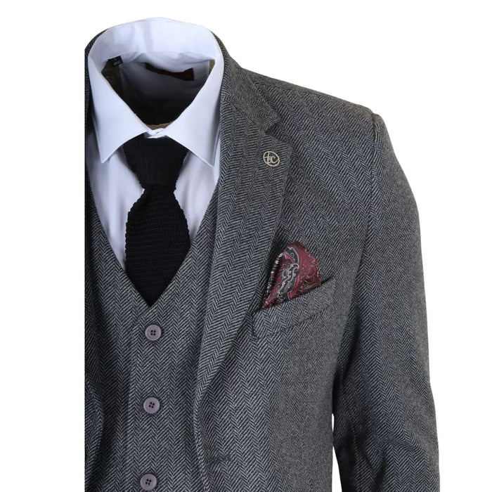 Men's grey 3 piece tweed herringbone suit with a tailored blazer, matching vest, and trousers, paired with a white dress shirt, black knit tie, and patterned pocket square for formal occasions.