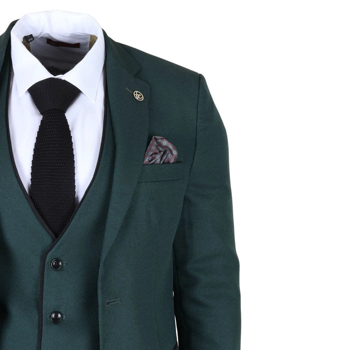 Men's dark green tailored fit suit jacket with a white dress shirt, black knit tie, and patterned pocket square, featuring a lapel pin and subtle textured fabric