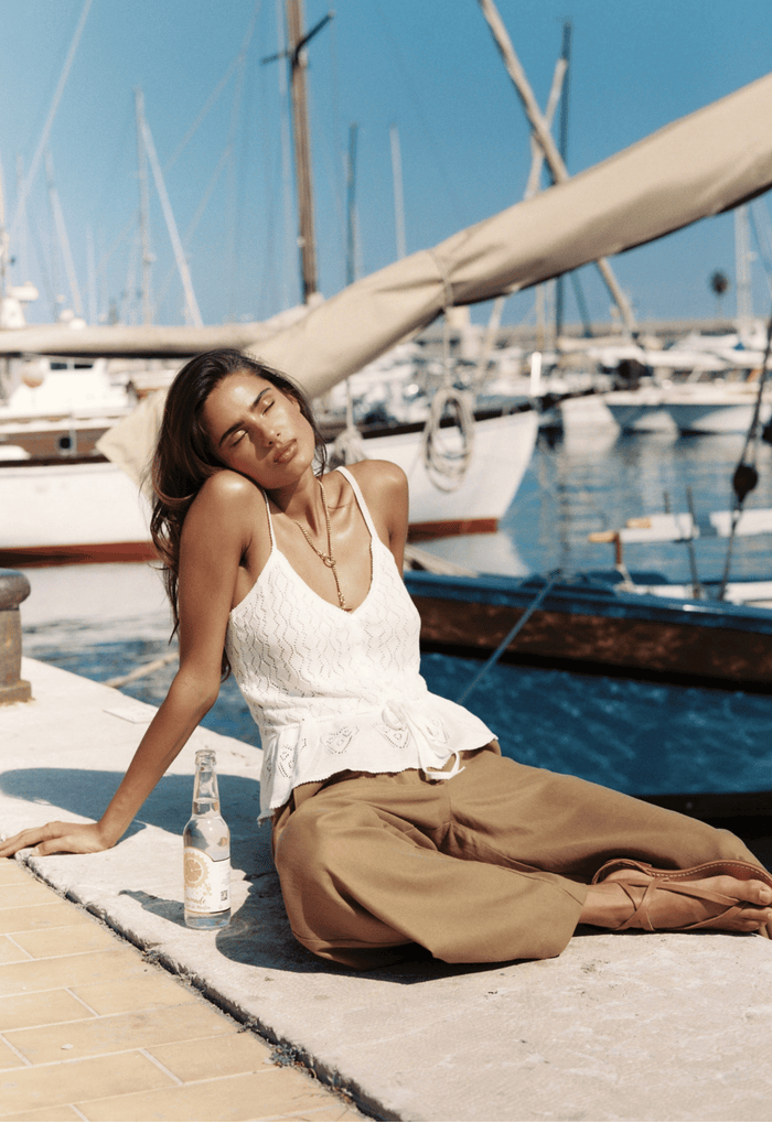 Model seated at a marina, front view of Jessa Pointelle Cami with waist tie and V-neckline in vintage cream