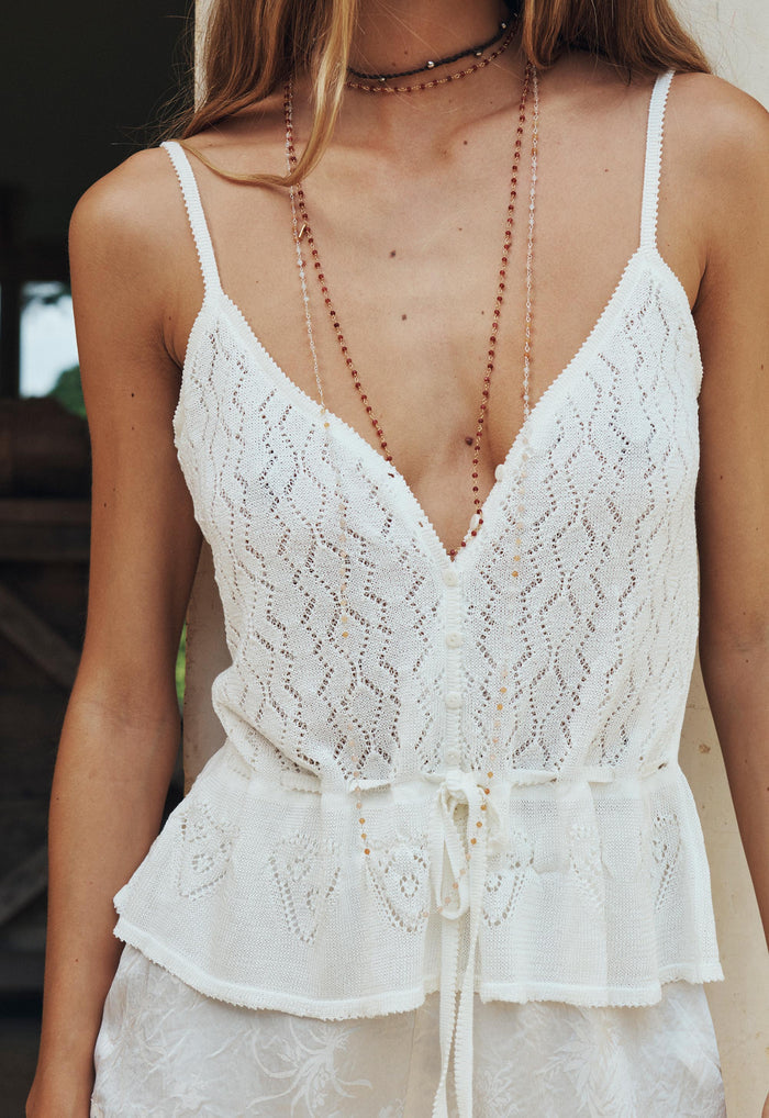 Front detail shot of pointelle knit cami showing deep V-neckline, button opening, and waist tie in vintage cream