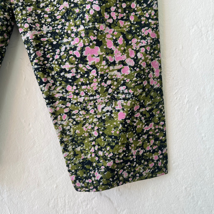Close-up of the lower leg of the kids lazy pants in green and pink speckle, showing the hand-printed Batiki cotton fabric with dark navy ground and scattered green, pink, and white speckle and splatter pattern with natural dye variation