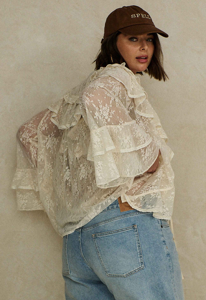 Back view of a model in cloud cream lace blouse, showing tiered fluted sleeves and sheer lace fabric with jeans