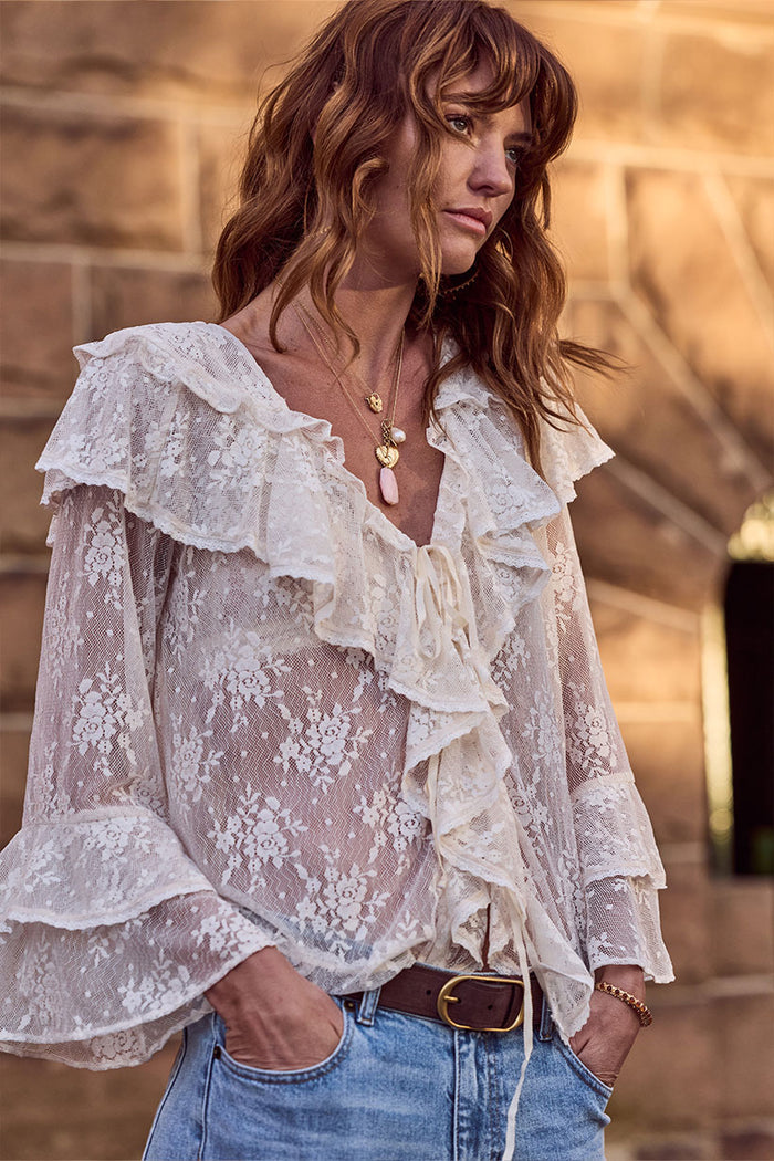 Cloud cream lace blouse laid flat showing front ties, neck ruffle, tiered fluted sleeves, and floral lace detail