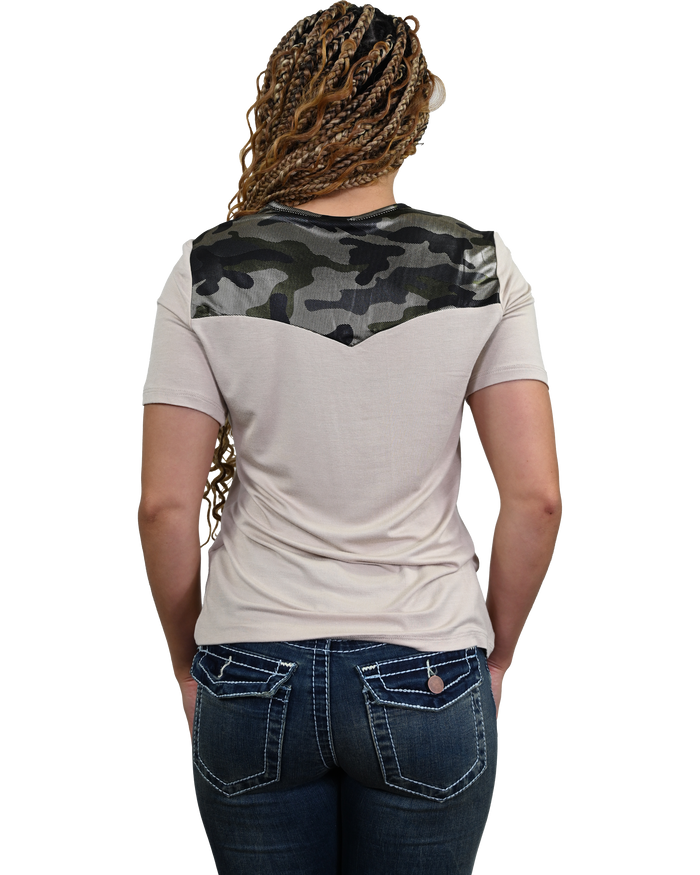 A woman viewed from behind wearing a short-sleeve t-shirt with a beige body and a dark green and black camouflage yoke across the shoulders, paired with dark blue jeans.