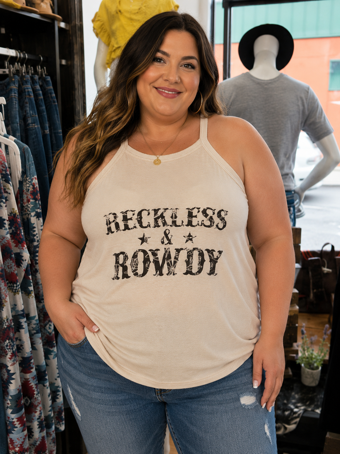 A woman wearing a cream-colored halter tank top with 'RECKLESS & ROWDY' printed in distressed black lettering, paired with blue jeans, standing inside a clothing store.