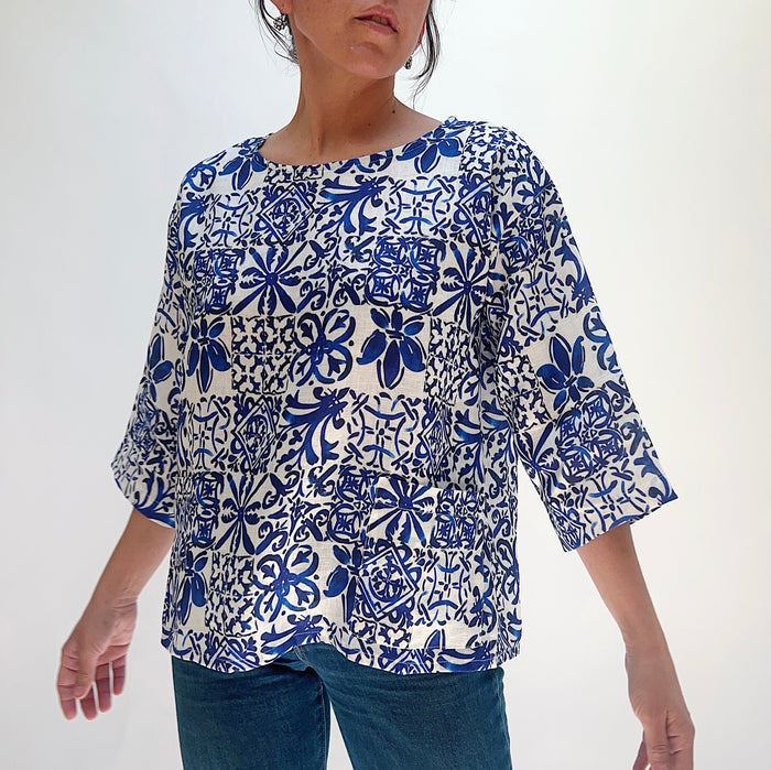 Full front view of the Christopher Calvin Linen Blue Tiles Print Top with blue-and-white Moroccan tile print, relaxed fit, boat neckline, and 3/4 sleeves, worn with blue jeans on a white background